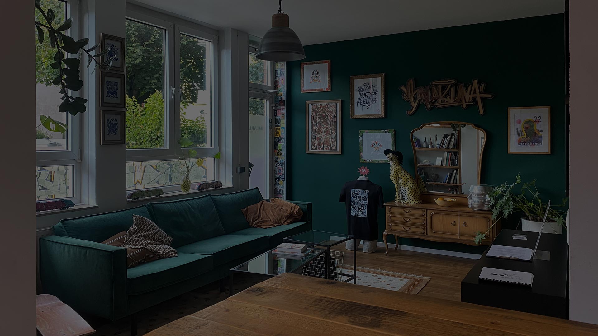 Gemütlicher Wartebereich im Balaklava Tattoo Studio mit grüner Wand, Sofa, Kunstwerken und Tageslicht in Münster