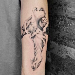 Surrealistisches Black & Grey Tattoo mit zwei Schwänen auf menschlicher Figur und fließender Draperie, gestochen von Jona bei Balaklava Tattoo Münster. Surreal black and grey tattoo of two swans merged with a human figure and flowing drapery, tattooed by Jona at Balaklava Tattoo Münster.